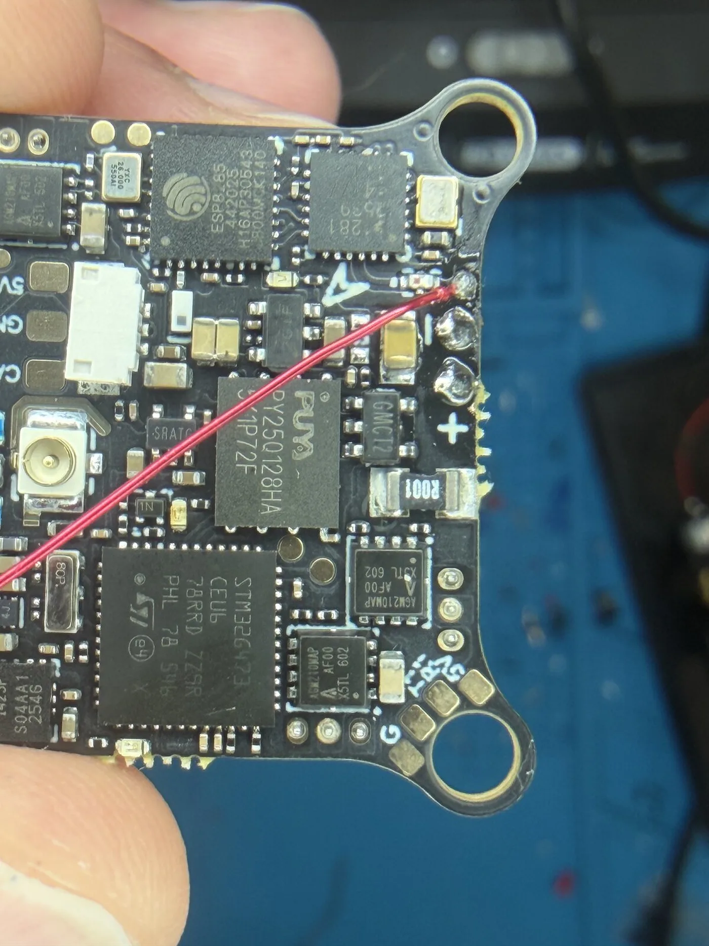 Close-up of a BetaFPV Matrix 1S flight controller held in fingers, with its red antenna wire