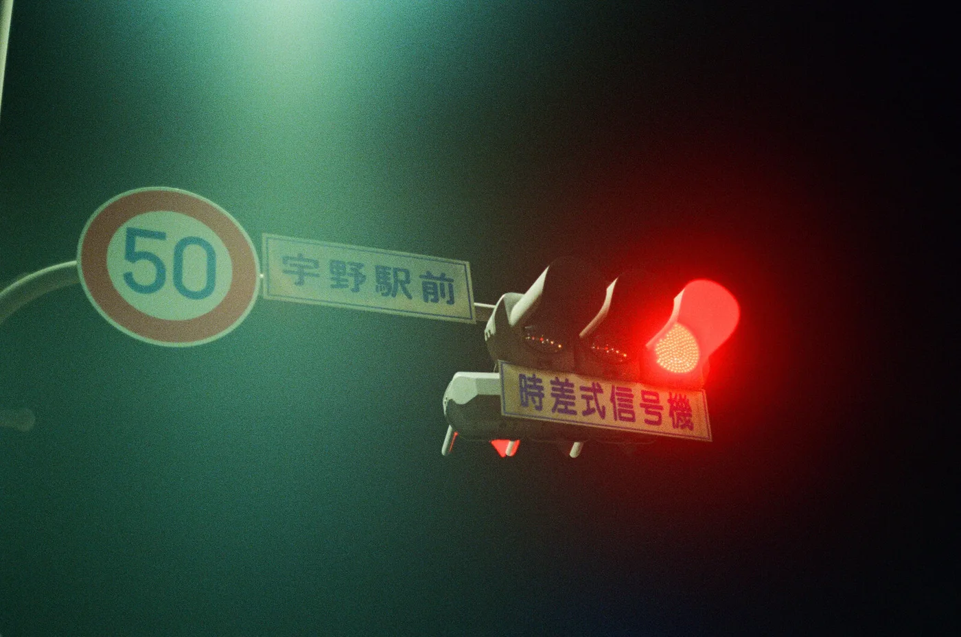 A Japanese traffic light glowing red next to a 50 km/h sign, at dusk