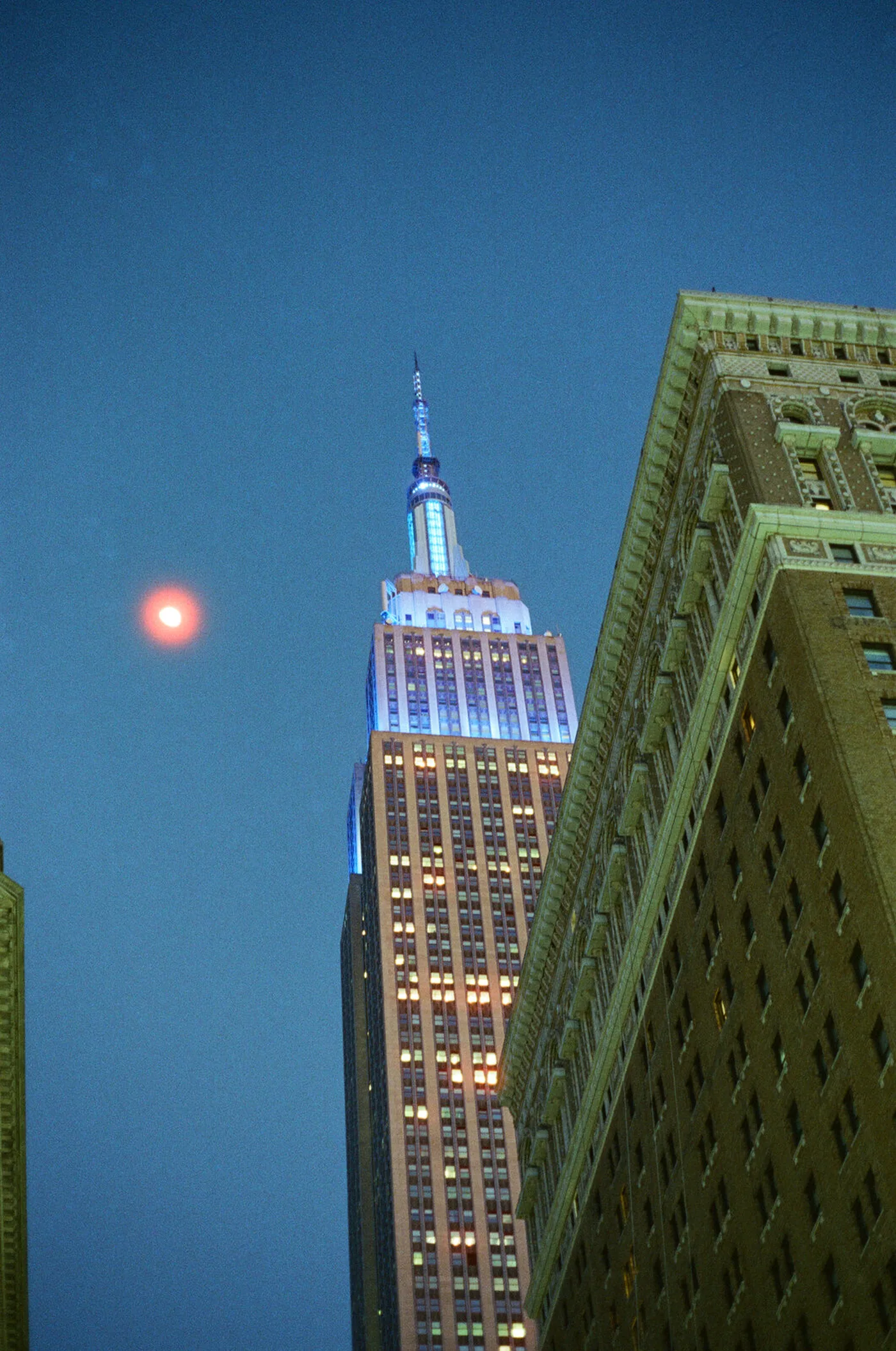 The Empire State Building lit at dusk, with the moon beside it