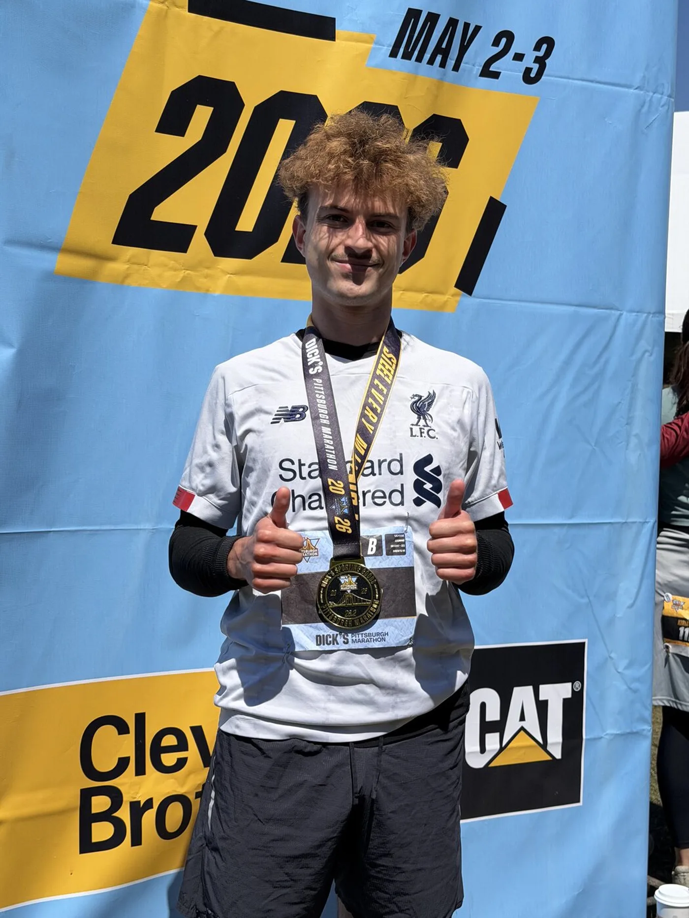 Me with my finisher medal in front of the Pittsburgh Marathon 2026 banner, two thumbs up