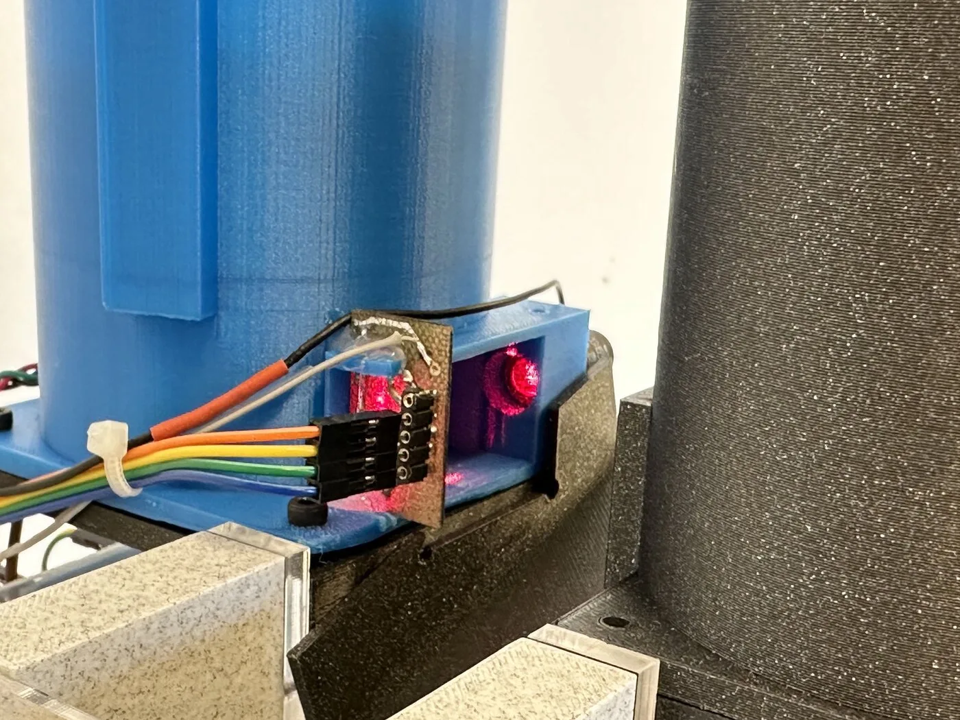Close-up of a small board with a red light at the outlet of the blue hopper