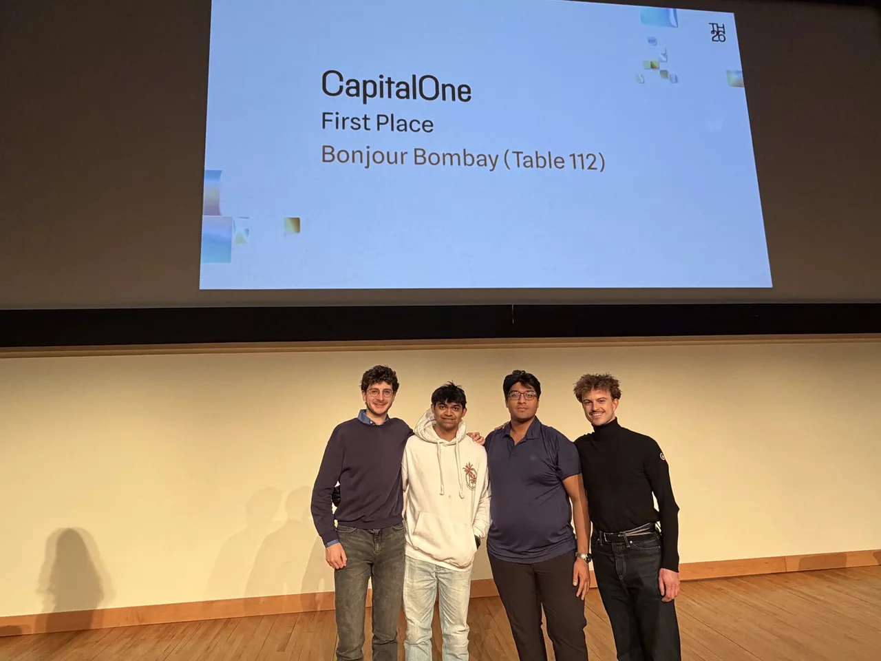 Four team members on stage under a screen reading CapitalOne First Place, Bonjour Bombay