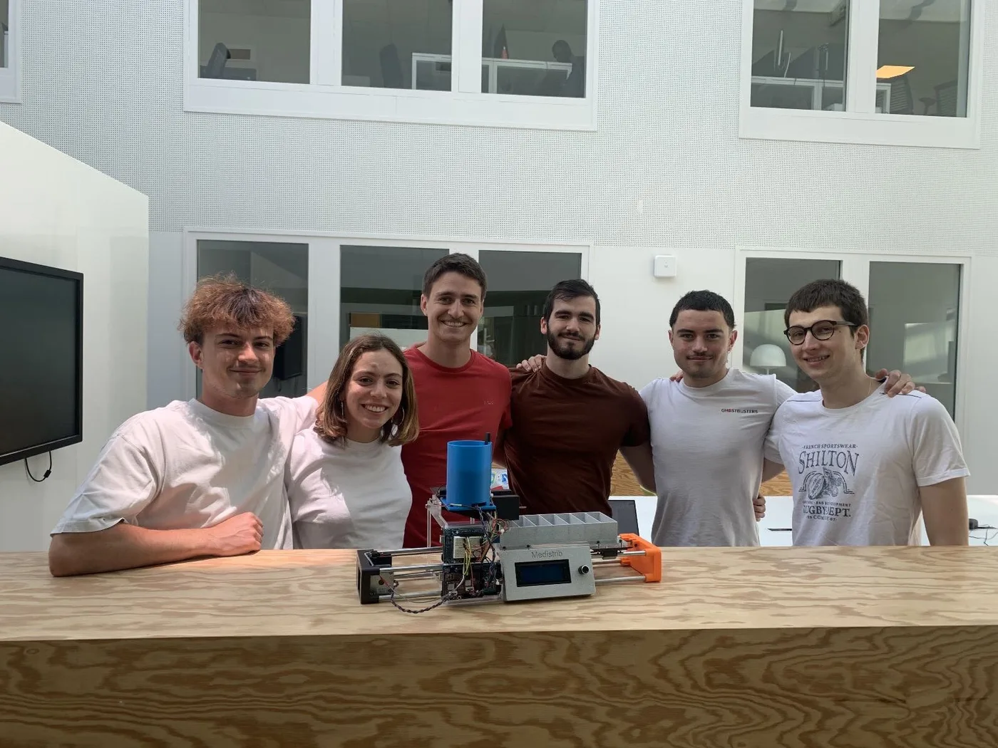 Six students smiling behind the Medistrib prototype on a wooden counter